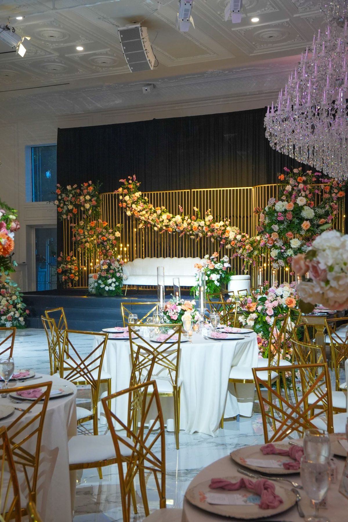 A floral stage and reception tables in a ballroom styled by New Era Events