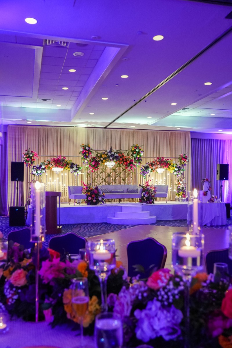 A ballroom stage with bright pink, orange and purple florals and candlelight, designed by New Era Events