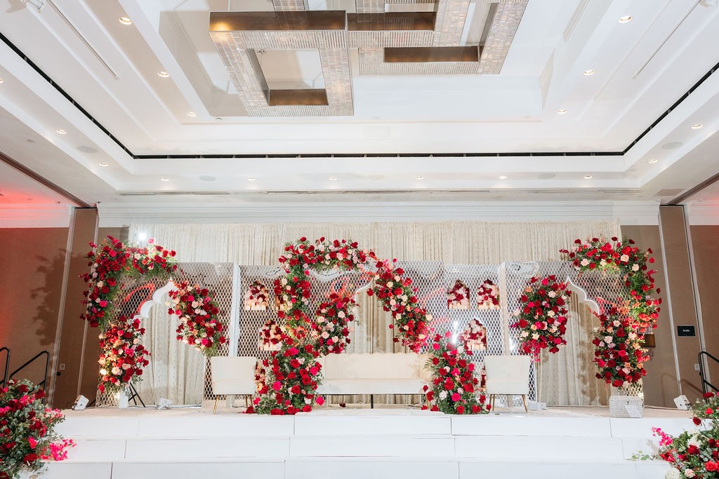 A white stage with red and pink rose arches and white lounge seating, designed by New Era Events