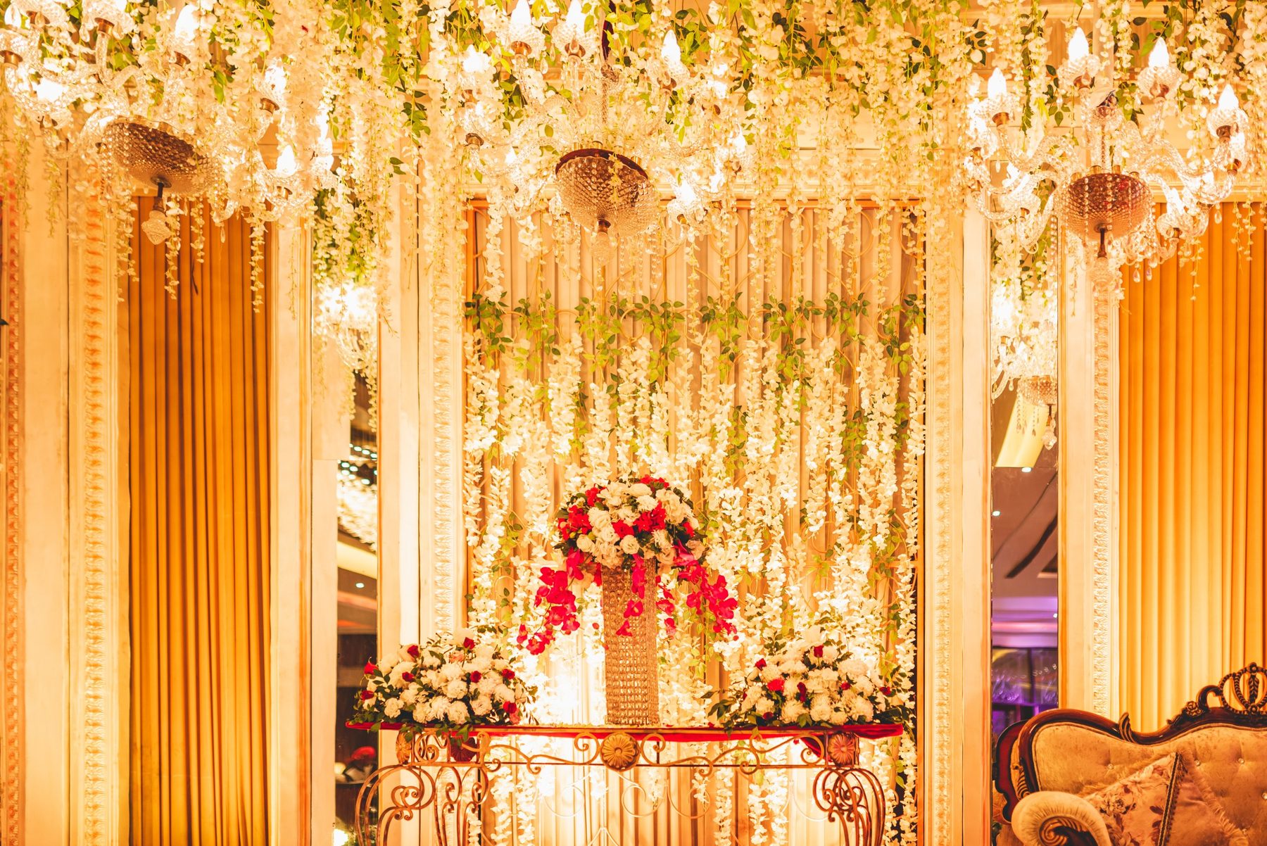 A ballroom stage with crystal chandeliers, hanging white florals and a red and white centerpiece at The Amberlight Ballroom