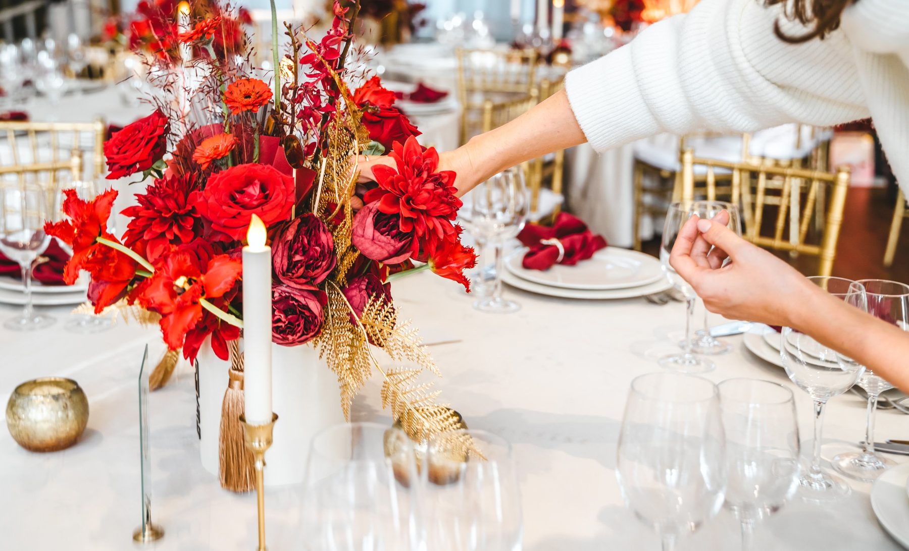 A planner arranging a red and gold floral centerpiece on a reception table